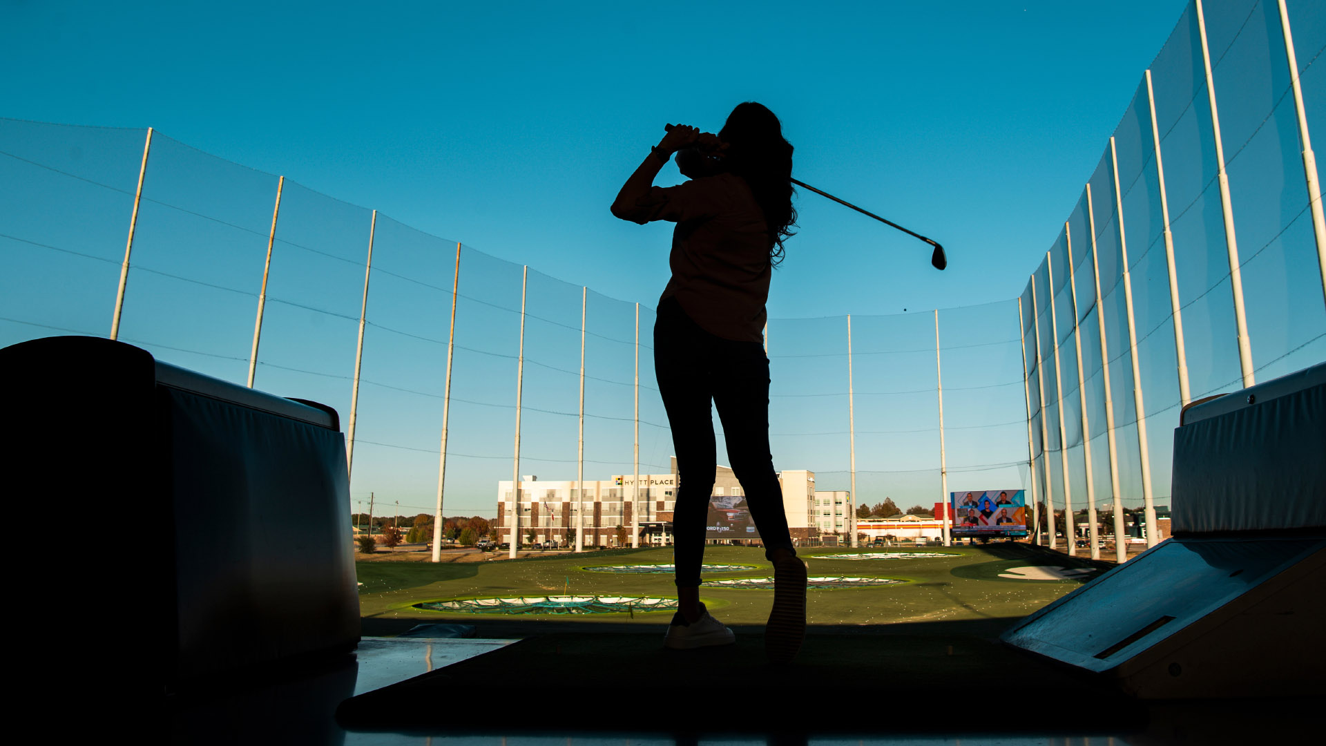 Woman swinging golf club inside a bay at Topgolf