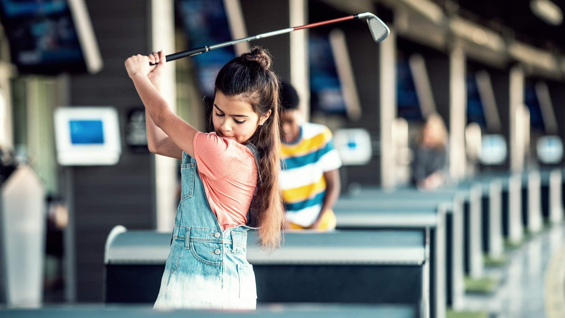 Young girl swinging golf club in a bay at Topgolf