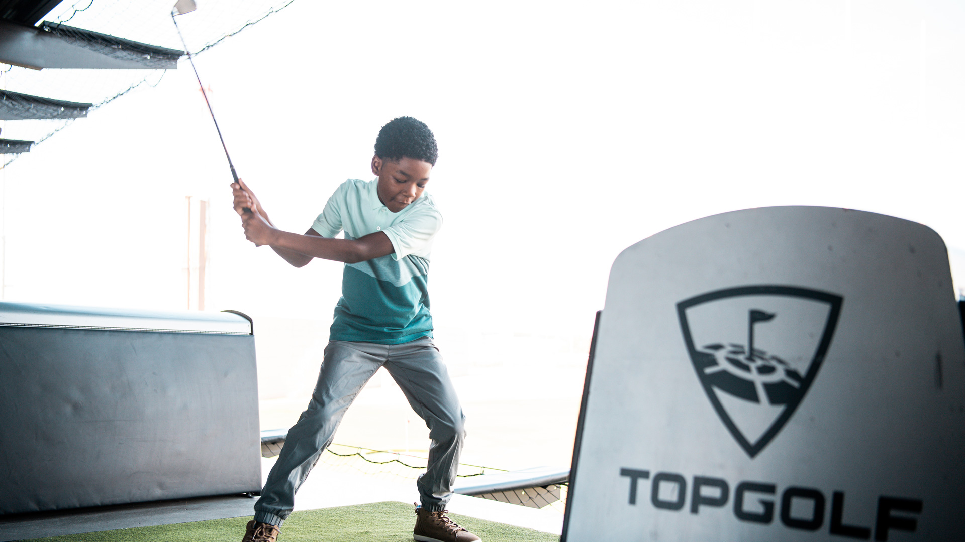 Child swinging golf club inside a bay at Topgolf